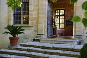 Un edificio de piedra con una serie de escalones que conducen a una puerta, una planta en maceta y una ventana con barrotes.