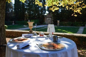 Mesa redonda al aire libre con platos, vasos y una vela.