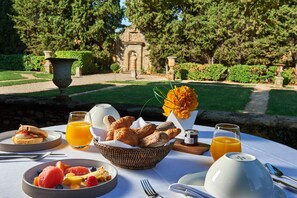 Un desayuno con una mesa para dos, con croissants, fruta y jugo de naranja.