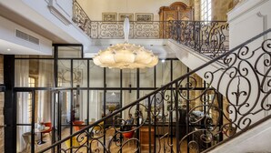 Un magnifique escalier orné de rampes noires travaillées, un lustre et une vue sur une salle à manger située en contrebas.