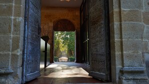 Un couloir en pierre, avec une porte en arc donnant sur un jardin.