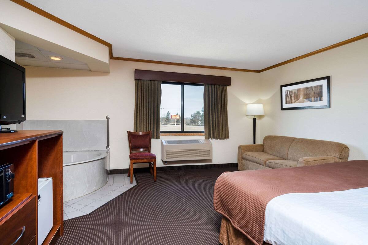 A hotel room with a bed, a sofa, a chair, a desk with a television, a window with curtains, and a picture on the wall.