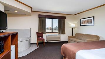 A hotel room with a bed, a sofa, a chair, a desk with a television, a window with curtains, and a picture on the wall.
