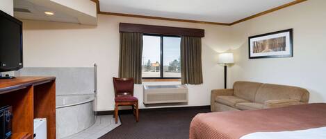 Una habitación de hotel con cama, sofá, sillón, escritorio con televisor, ventana con cortinas y un cuadro en la pared.