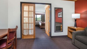 Una habitación de hotel con una mesa de comedor de madera, un sofá, un espejo y una cama con cortinas.