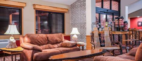 A spacious living area with leather sofas, a coffee table, and a fireplace. There are two lamps on side tables, and a brick wall adds a rustic touch.