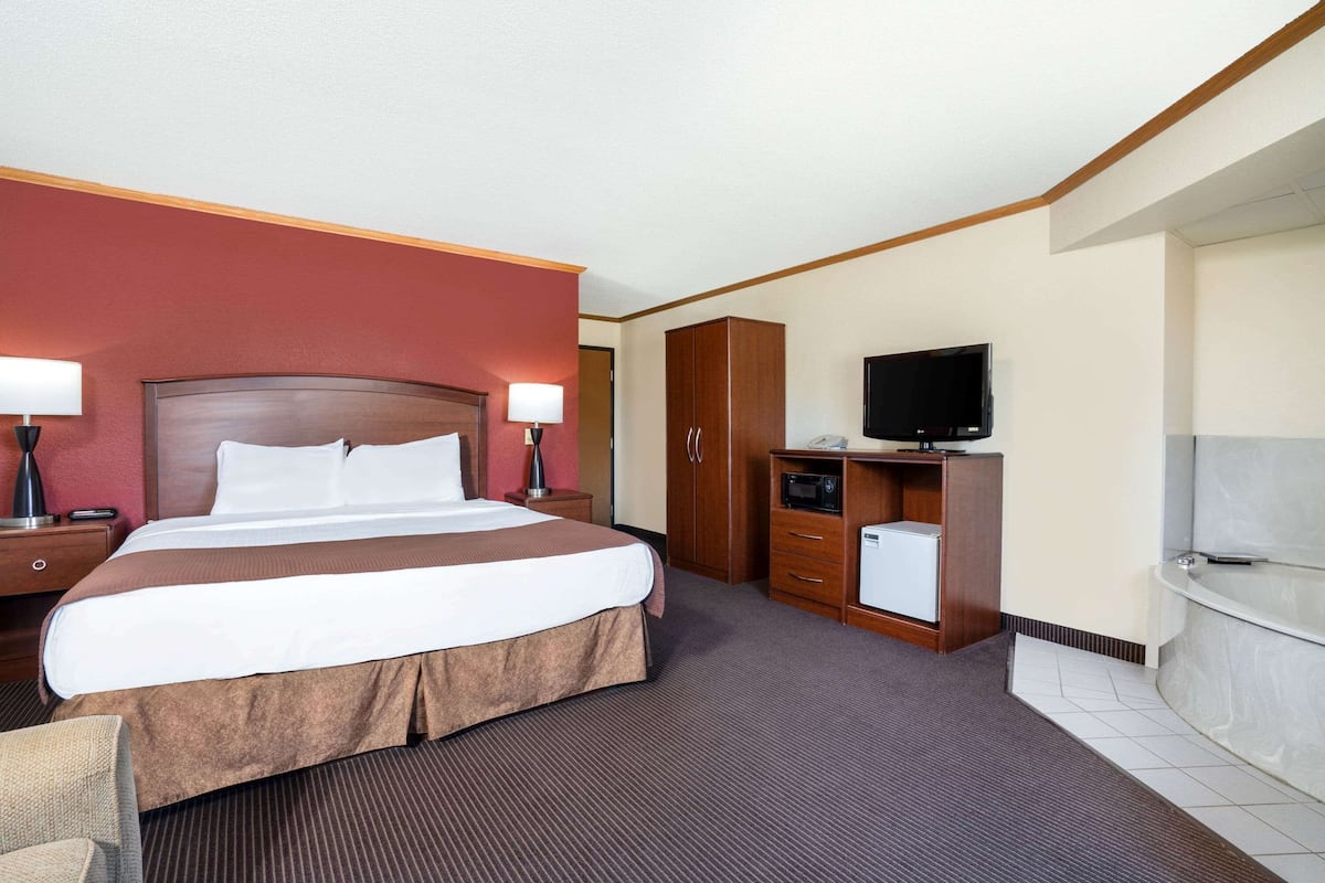 A hotel room with a large bed, a desk with a lamp, a television, a microwave, and a bathroom with a bathtub.
