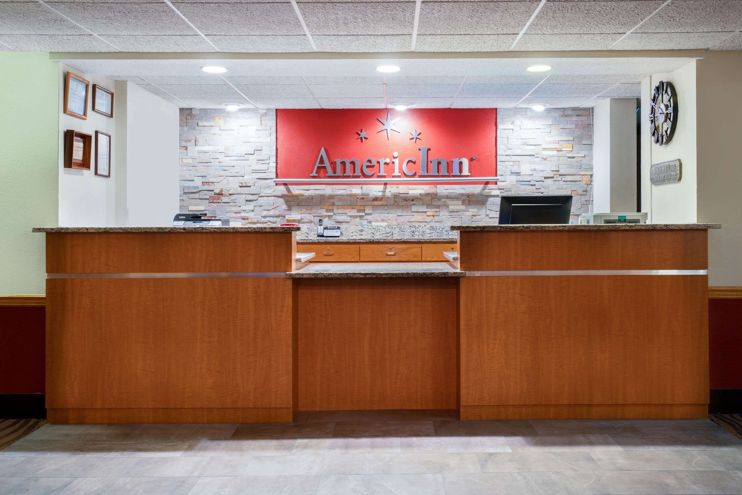 A reception desk with a red sign reading "AmericInn" and a clock on the wall.