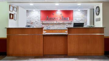 Eine Rezeption mit einem roten Schild, das "AmericInn" zeigt, und einer Uhr an der Wand.