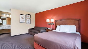 A hotel room with a bed, a chair, a desk with a lamp, a telephone, and a mirror.