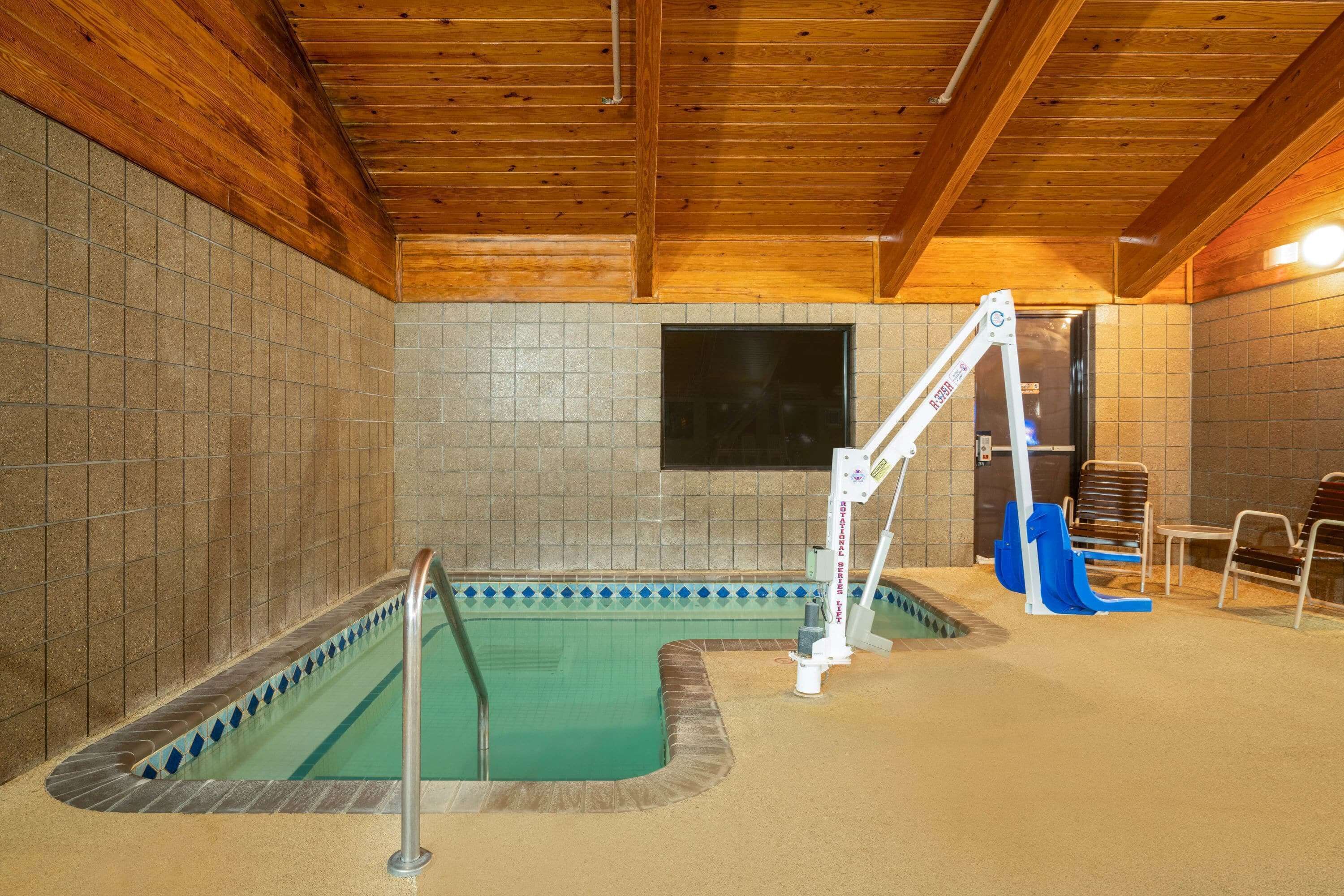 Piscina com trampolim e cadeiras, cercada por paredes azulejadas e vigas de madeira.