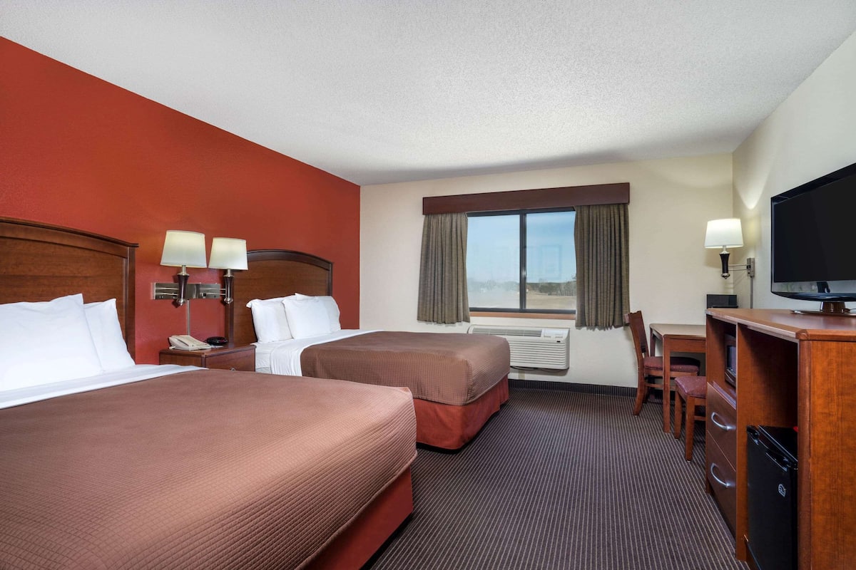 A hotel room with two beds, a desk, a television, and a window with curtains.
