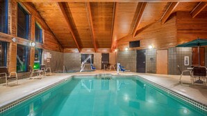 Piscina interior con vigas de madera, paredes de azulejos y una silla de socorrista.