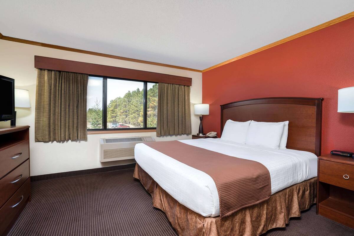 A hotel room with a large bed, a desk with a lamp, a TV, and a window with curtains.