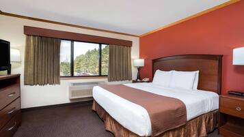 A hotel room with a large bed, a desk with a lamp, a TV, and a window with curtains.