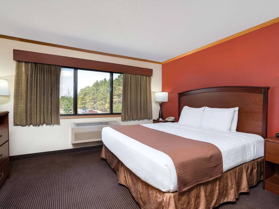 A hotel room with a large bed, a desk with a lamp, a TV, and a window with curtains.