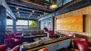 A cozy lounge area with leather sofas and chairs, a stone wall, and a large wooden artwork. - Glacier Bay Lodge (Gustavus)