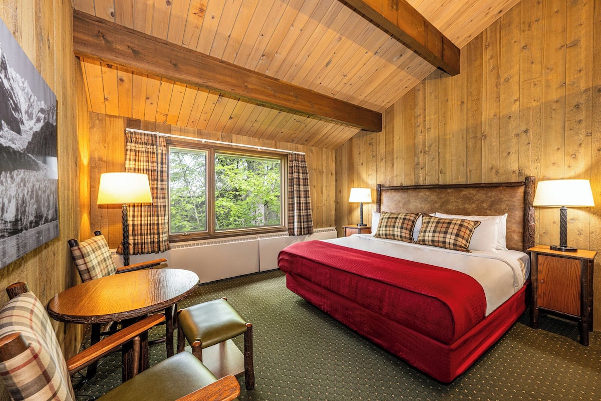 A wooden room with a bed, two nightstands, a table, and chairs.