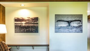 A hotel room with a bed, a red throw blanket, a lamp, and two wall-mounted pictures depicting a sunset and a whale tail. - Glacier Bay Lodge (Gustavus)