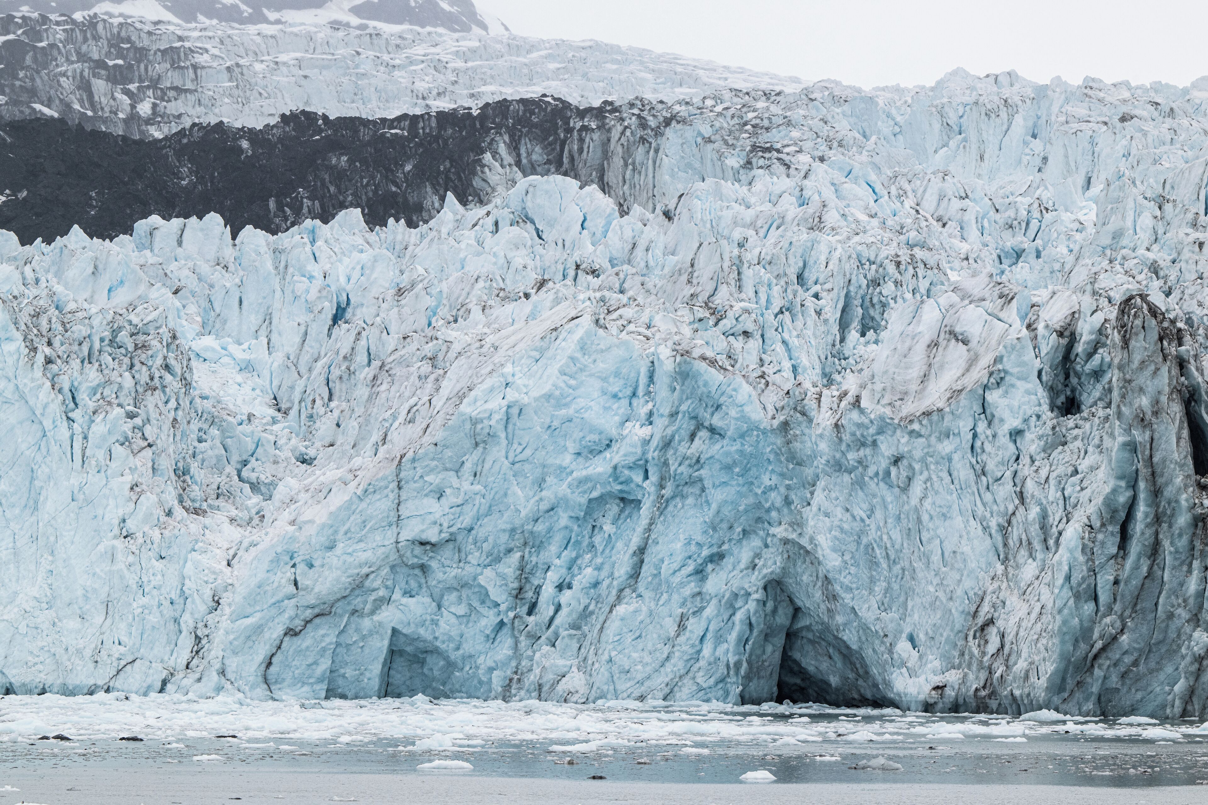 Un glacier à la surface accidentée, recouverte de glace, et bordé d’une falaise rocheuse abrupte.