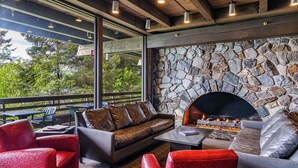 A cozy outdoor seating area with a stone fireplace, wooden beams, and a view of greenery. - Glacier Bay Lodge (Gustavus)