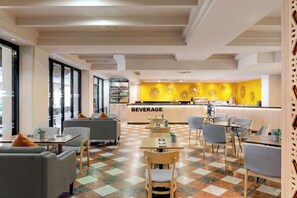 Een modern café met een centraal drankenbuffet, zitgedeeltes en een geruit vloertapijt.