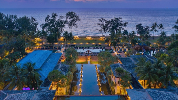 Un resort con piscina, palmeras y vista al océano al atardecer.