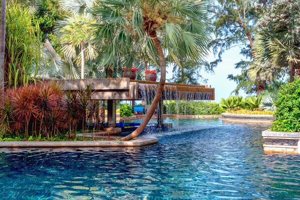 Un área de piscina con una cascada, rodeada de palmeras y diversas plantas.