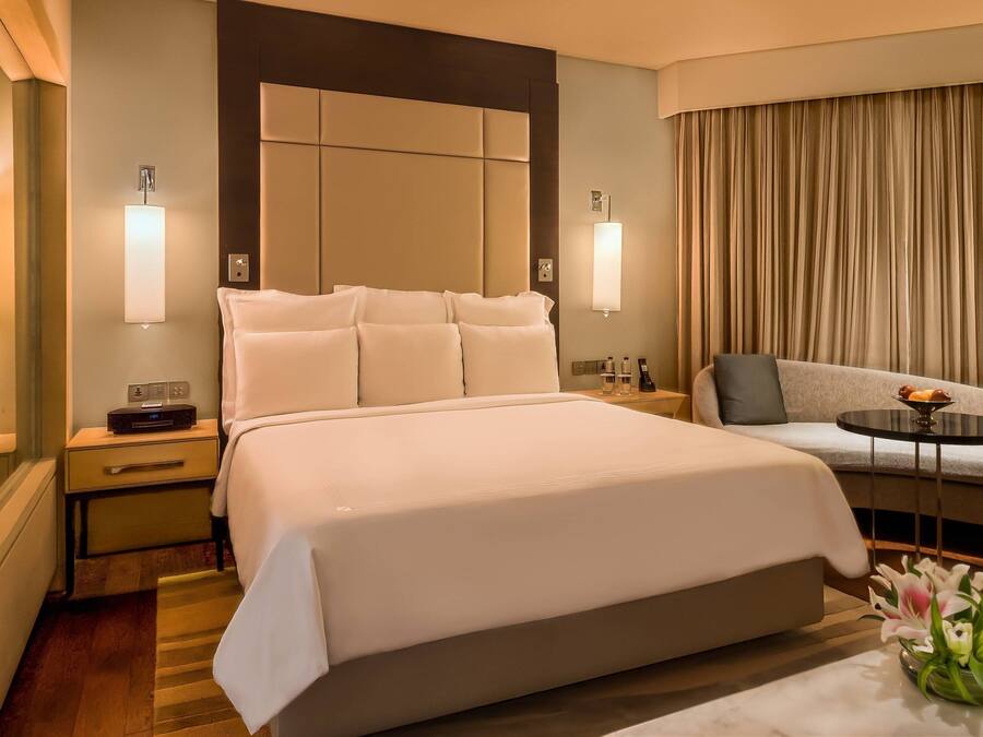 Habitación de hotel con una cama grande, un sofá, una mesita con frutero y un florero con flores.