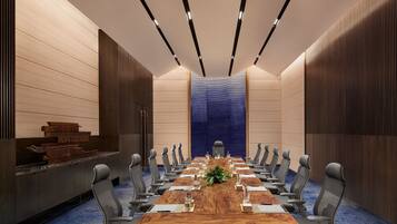 A conference room with a long wooden table, grey chairs, and a blue carpet.