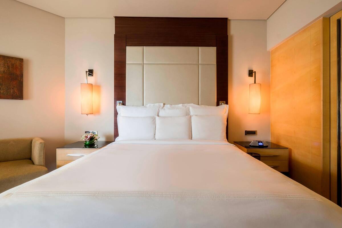Ein Hotelzimmer mit einem großen Bett, zwei Nachttischen, einer Sitzecke und Wandleuchten.