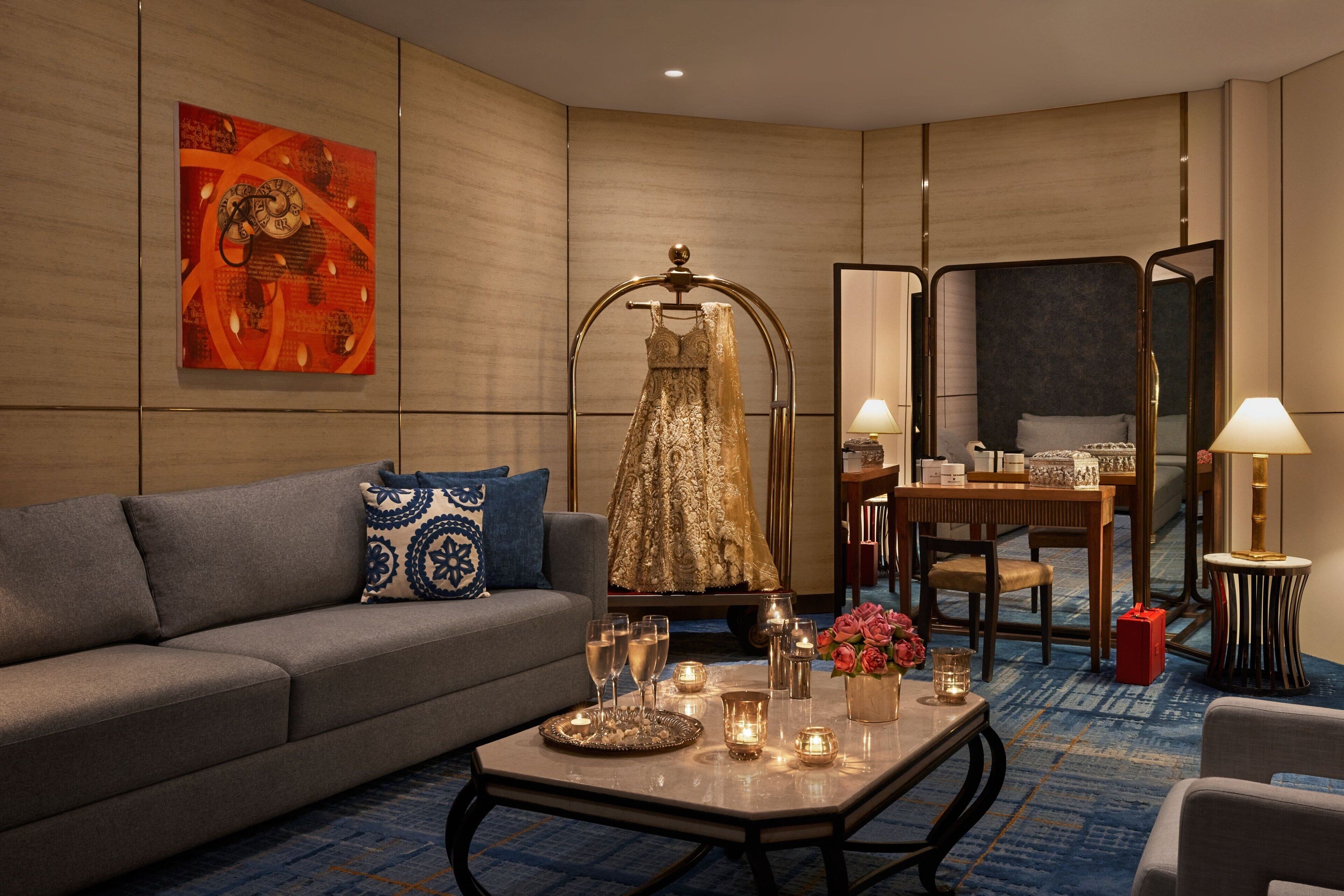 A hotel room with a sofa, a table with candles, a dress on a stand, and a mirror.