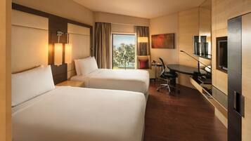 A hotel room with two beds, a desk, a chair, a TV, and a view of palm trees.