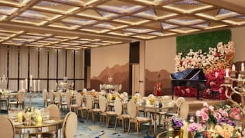 A banquet hall with round tables, chairs, and a stage with a piano.
