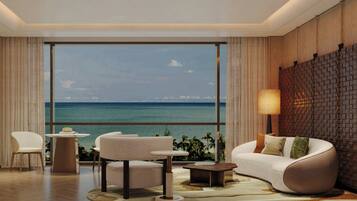 Sala de estar moderna com uma janela ampla com vista para uma praia, mobiliada com sofá, cadeiras e uma mesa pequena.