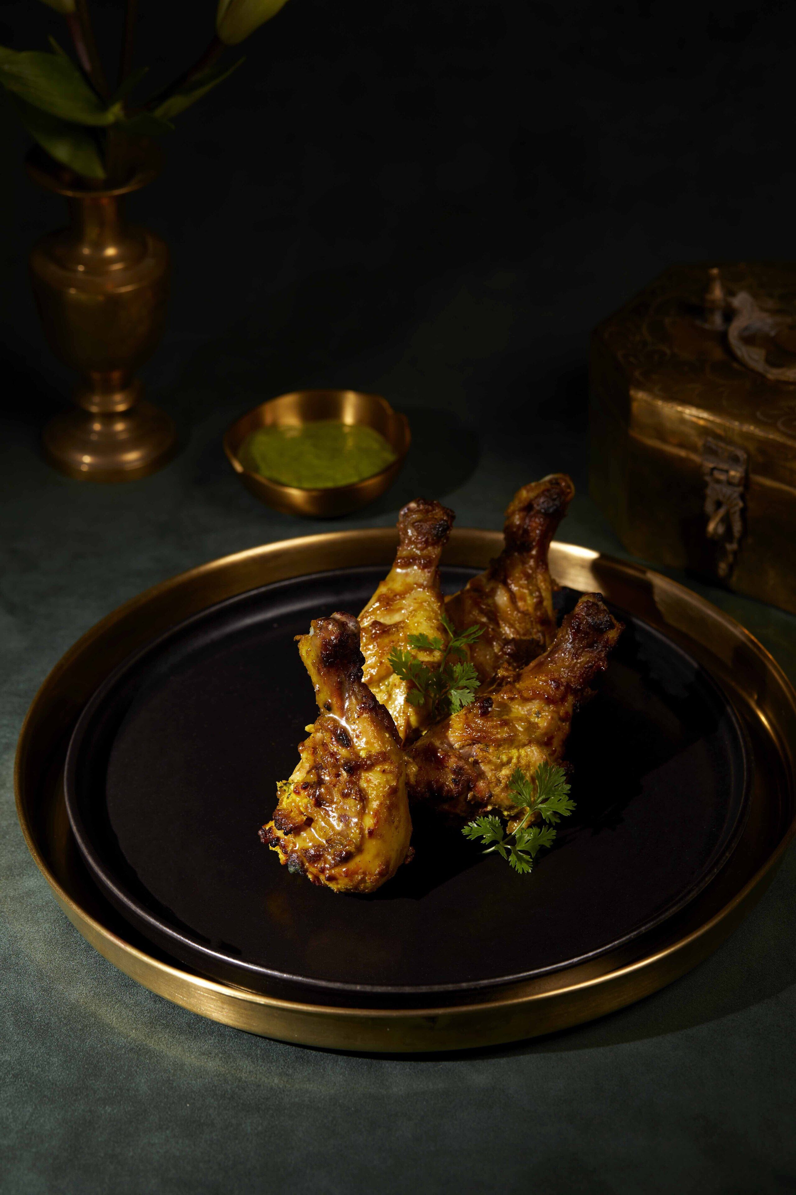 Ein Teller gegrillte Chicken Wings mit Garnitur, serviert auf einem schwarzen Teller mit goldener Kante.