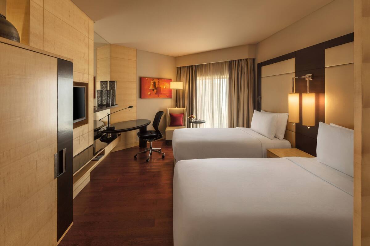 Ein Hotelzimmer mit zwei Betten, einem Schreibtisch mit Stuhl, einem Fernseher und einer Lampe.