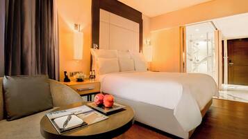 A hotel room with a large bed, a bedside table with a lamp, a sofa, and a small round table with a magazine and a pen.