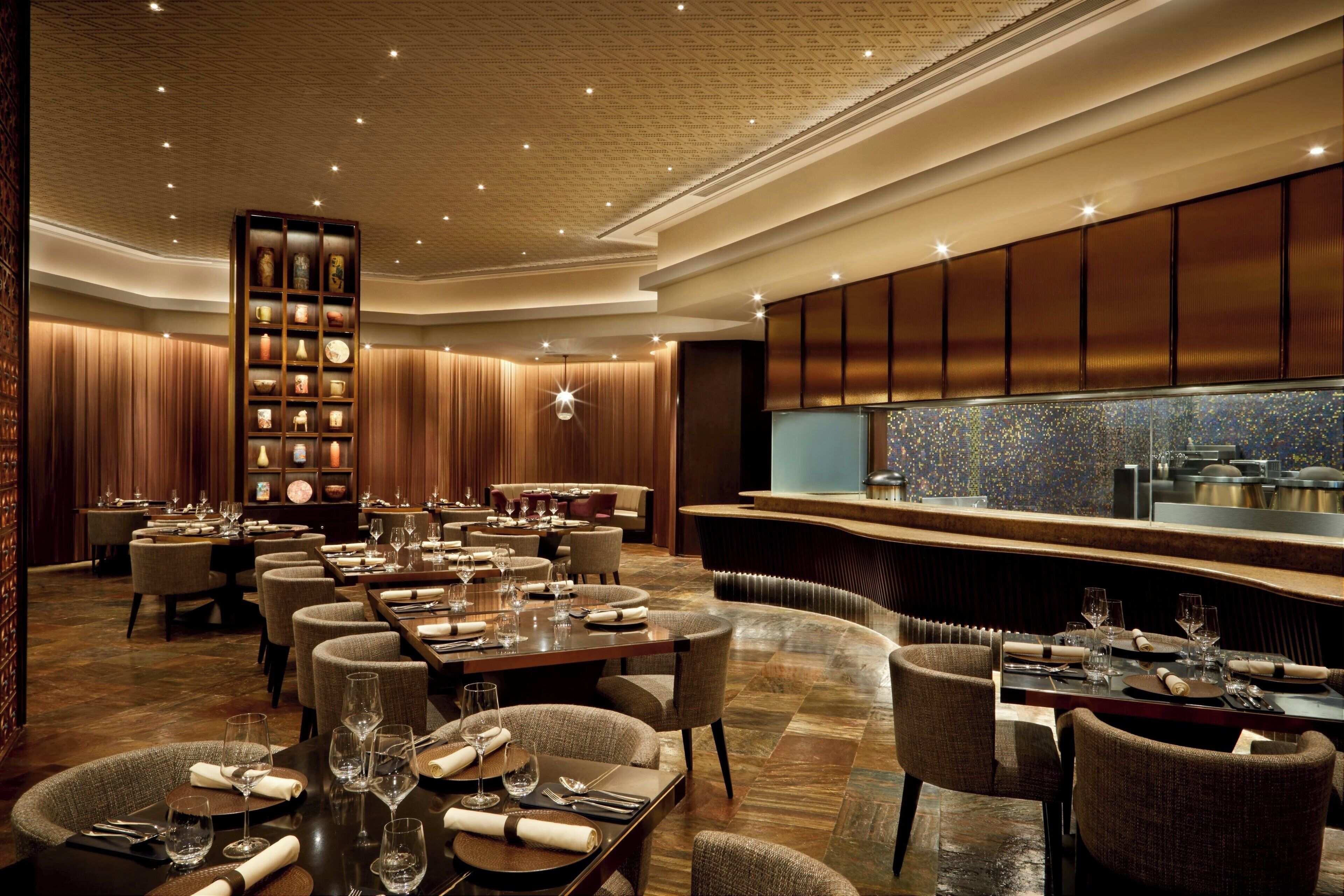 A spacious restaurant with multiple dining tables, a central bar area, and a decorative bookshelf.