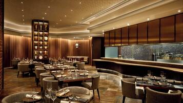 A spacious restaurant with multiple dining tables, a central bar area, and a decorative bookshelf.