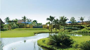 A landscaped garden with a pond, palm trees, and a building with a blue roof.