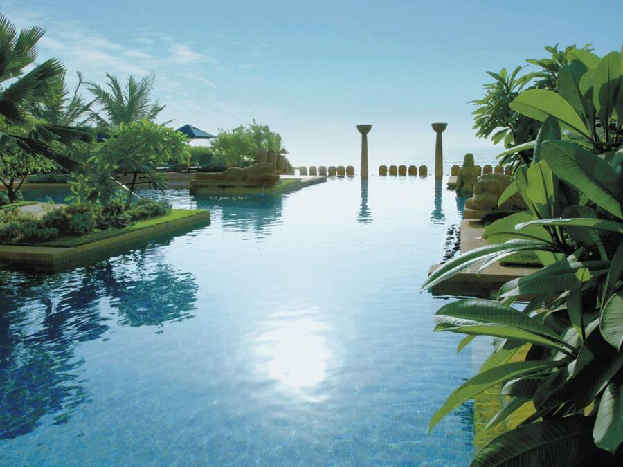 Piscina com águas cristalinas, cercada por plantas tropicais e palmeiras.