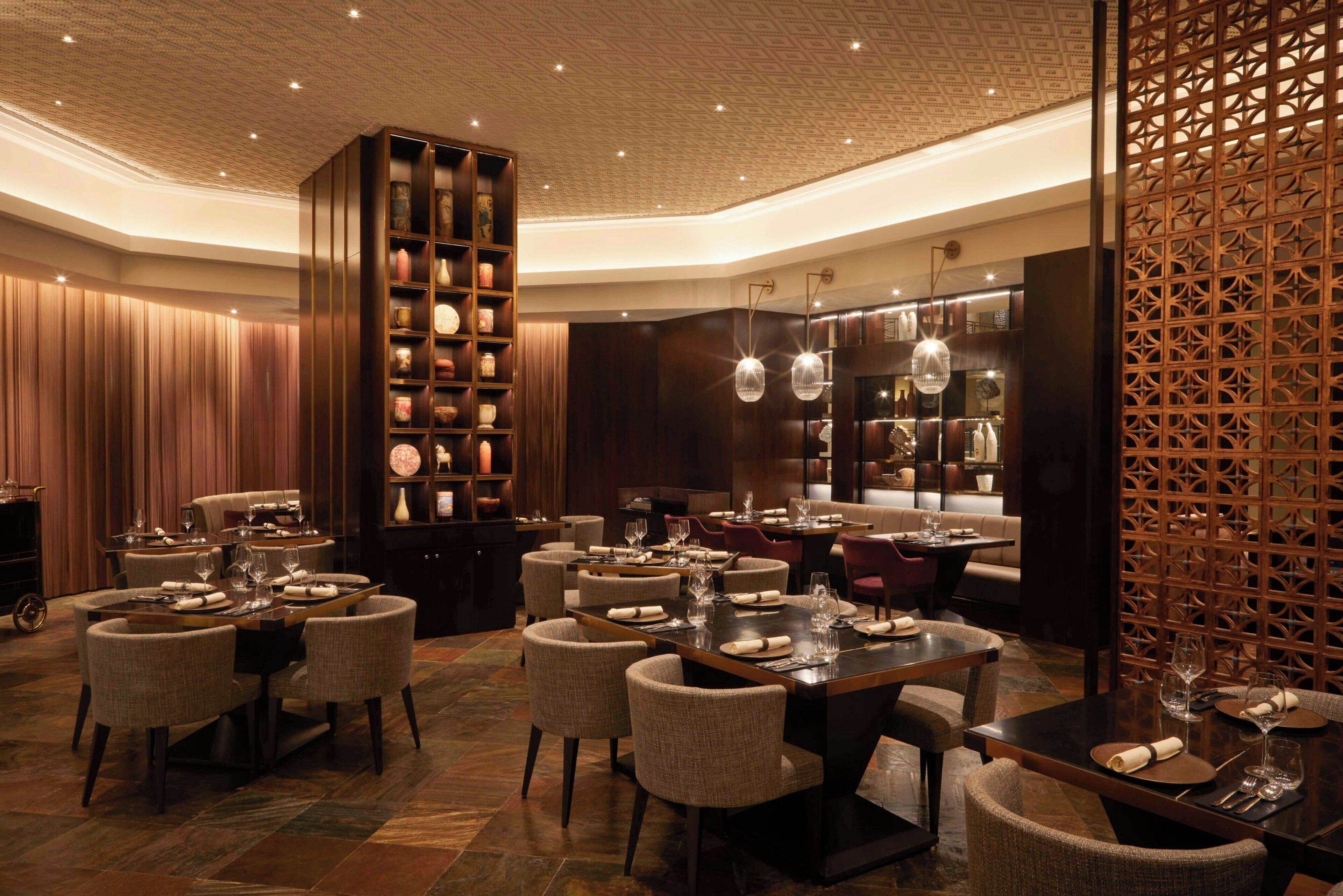 A luxurious dining area with multiple tables, elegant chairs, and a large wooden bookshelf.