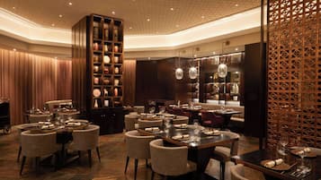 A luxurious dining area with multiple tables, elegant chairs, and a large wooden bookshelf.
