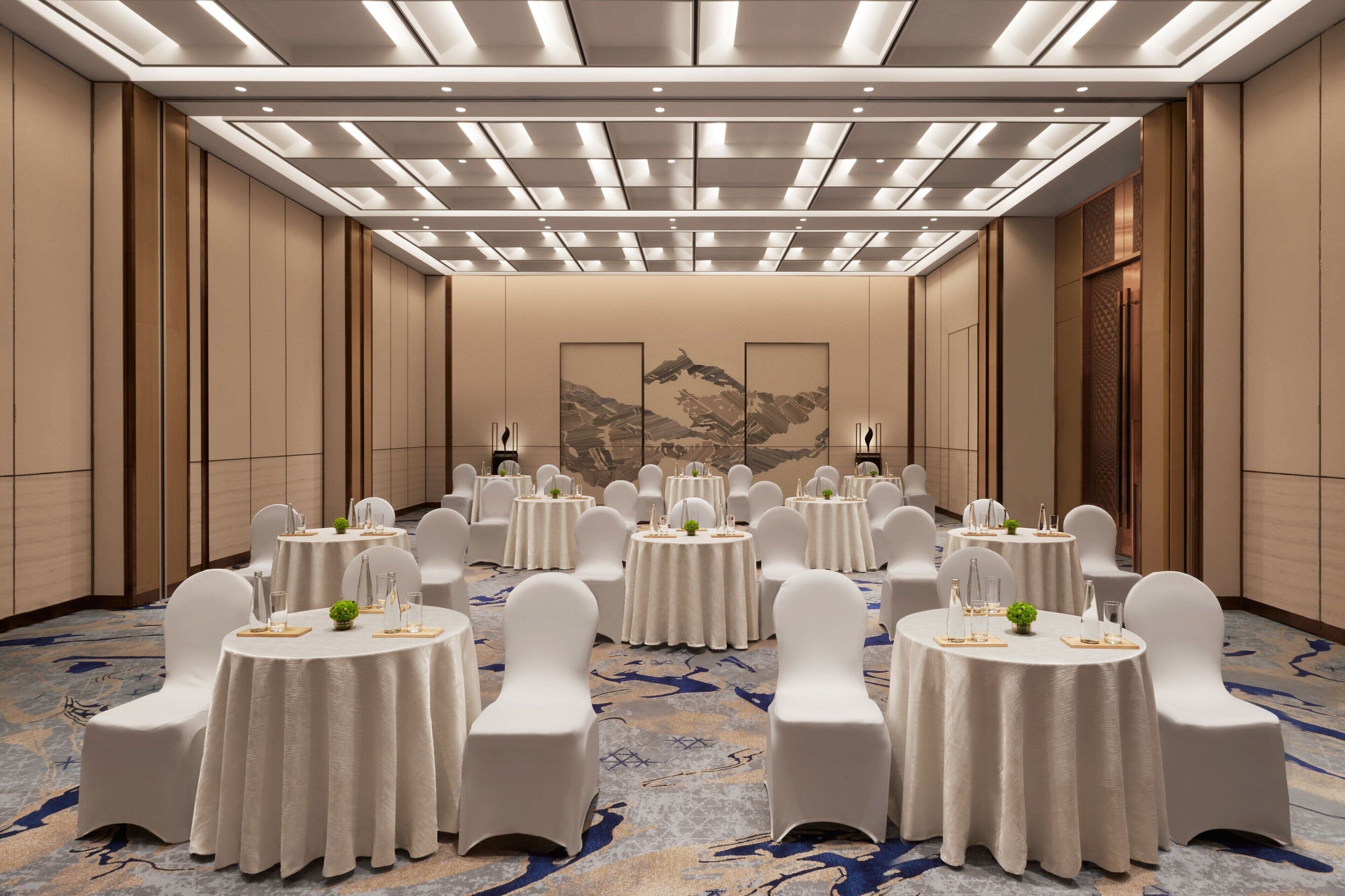A banquet hall with round tables, white chairs, and a patterned carpet.