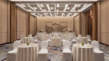 A banquet hall with round tables, white chairs, and a patterned carpet.