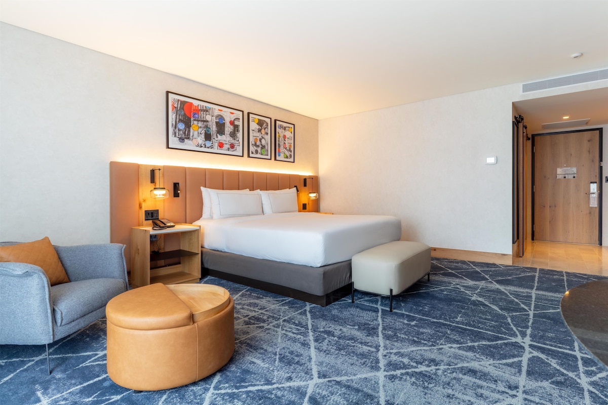 Una habitación de hotel con cama, mesita de noche, lámpara y un pequeño sofá.