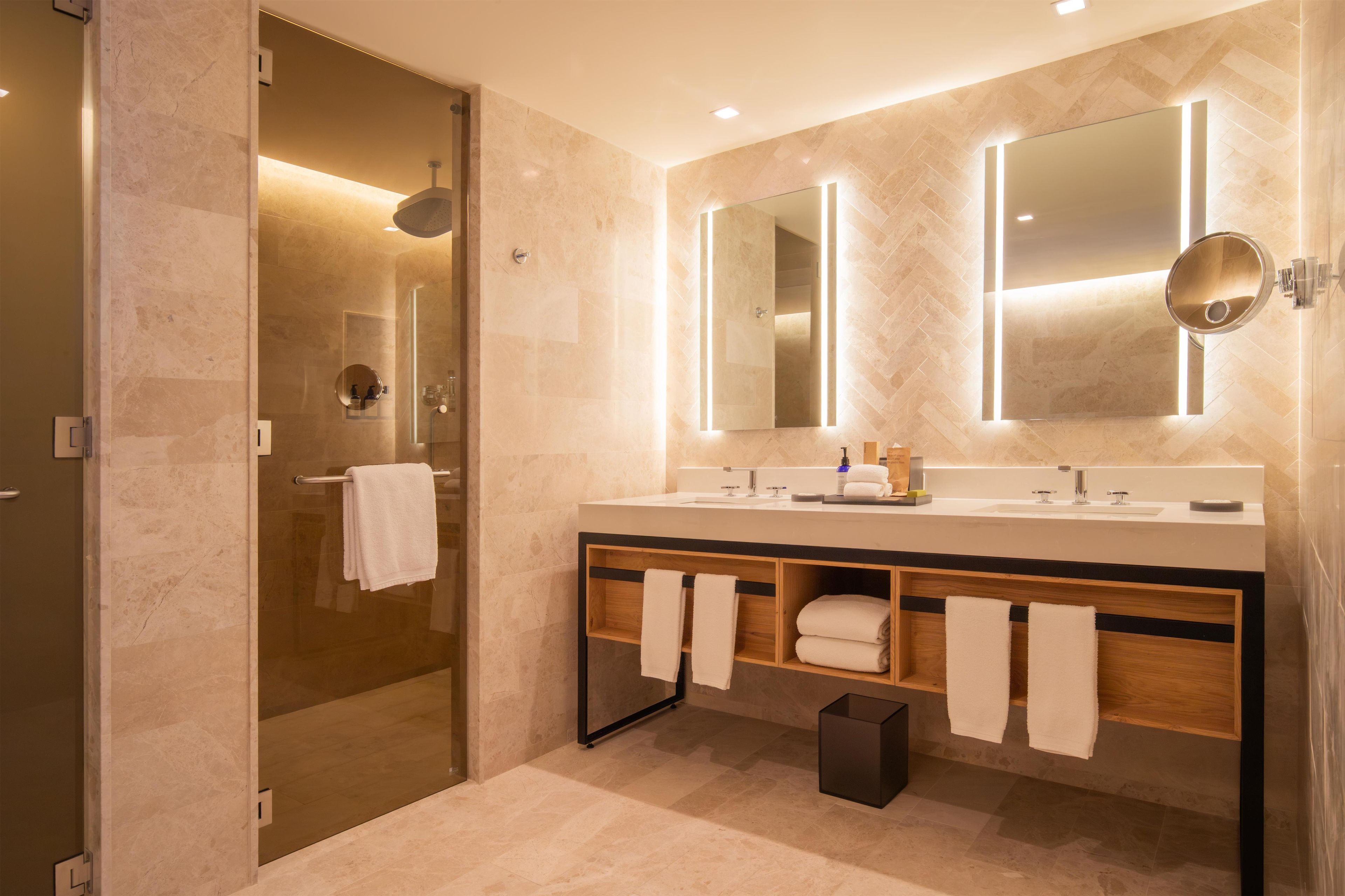 A modern bathroom with a glass-enclosed shower, a vanity with a mirror, and a wooden cabinet with towels.