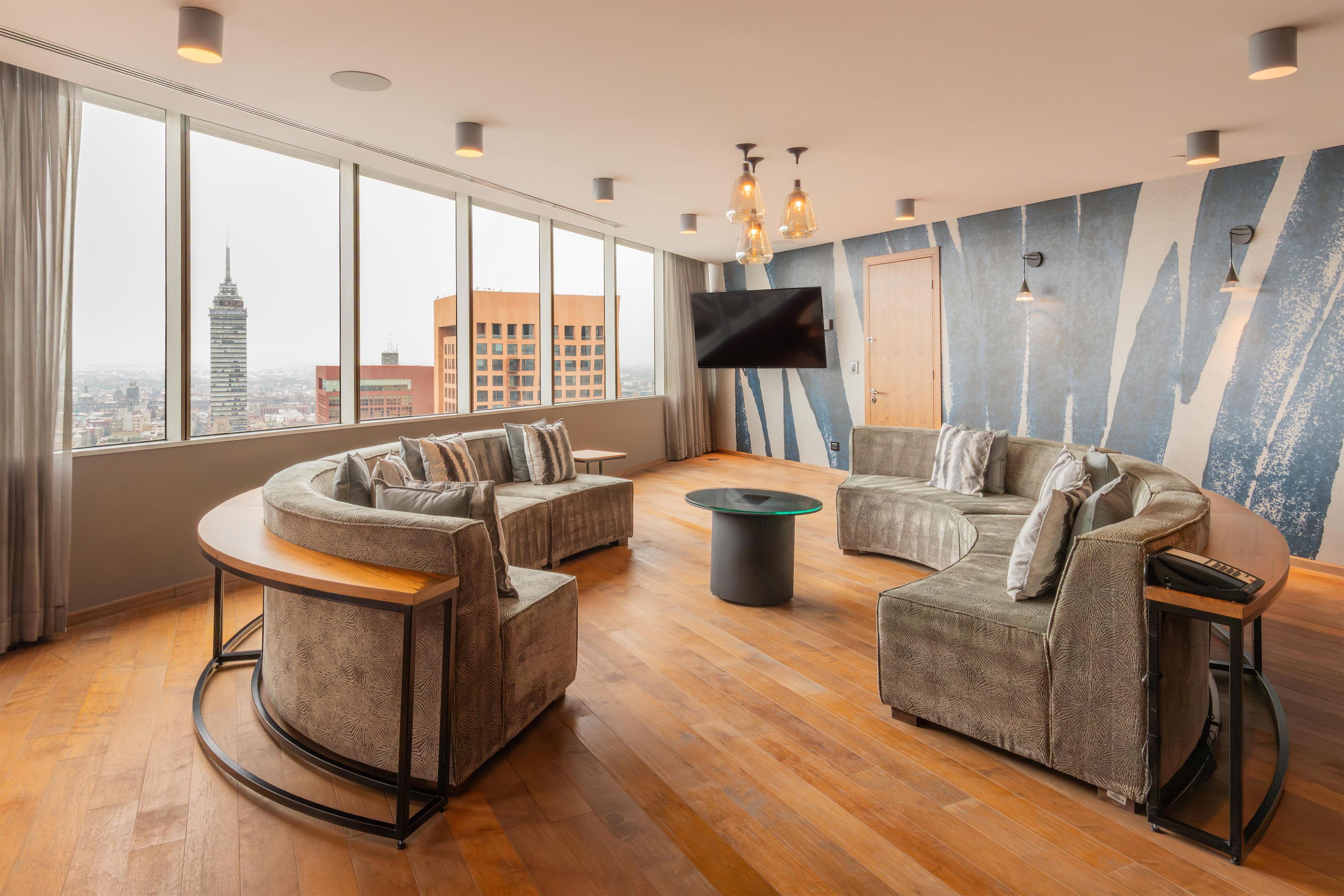 A modern living room with a curved sofa set, a flat-screen TV, and a city view.