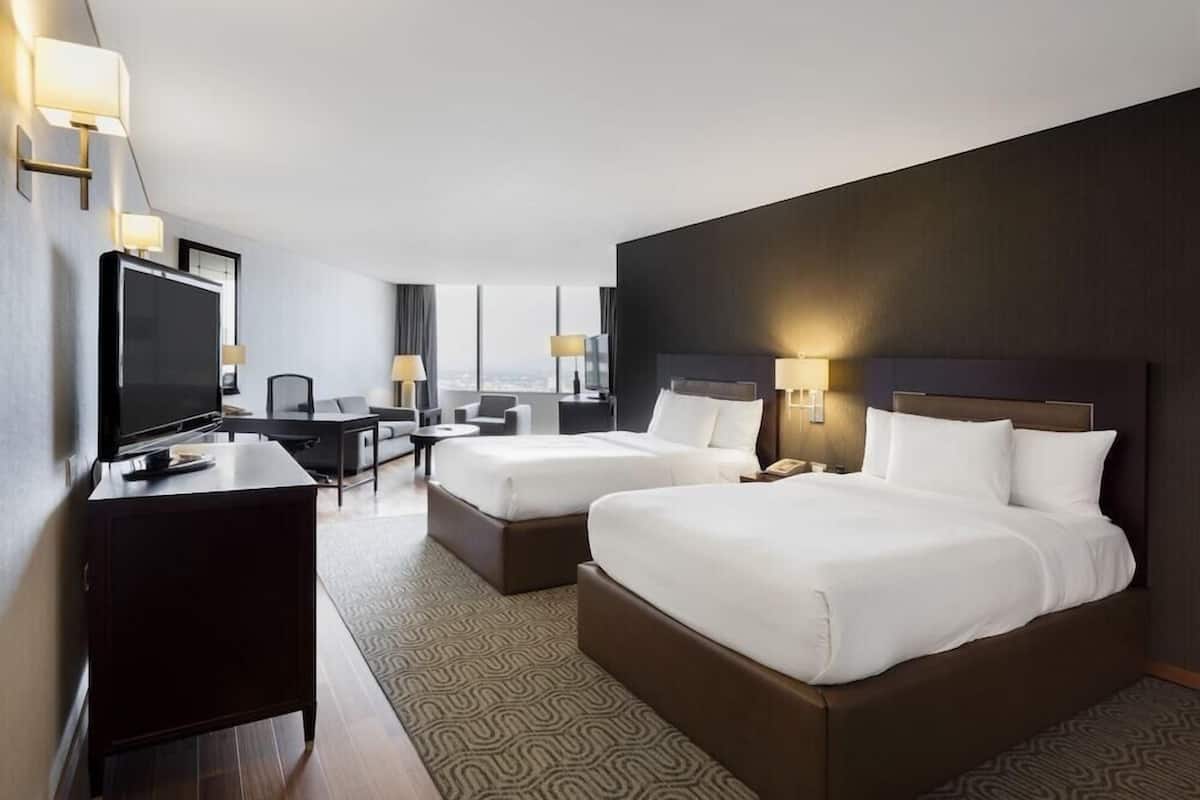 Habitació d'hotel amb dos llits, escriptori, televisió i vista a la ciutat.